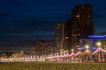 Evening lights twinkle along a beachfront promenade, with city high rises standing tall against the...