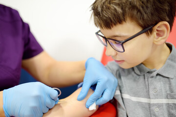 A nurse takes blood from a child using butterfly needle. Close up view of a boy's hand while taking a blood sample for examination in a modern laboratory or hospital.