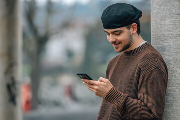 portrait of young man with mobile phone outdoors on the street wearing urban style cap - 785745105