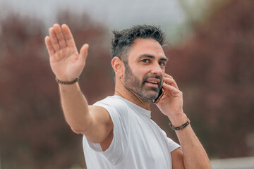 attractive young adult man with beard outdoors talking on mobile phone and waving