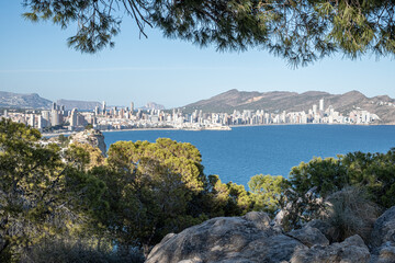 Panoramic view of a coastal city skyline seen from a verdant hilltop, a fusion of urban and natural...