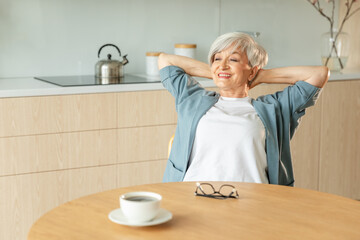 Senior old woman feeling relaxed stretching arms in kitchen at home. Smiling mature woman...