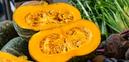 Orange squash cut in half with seeds, surrounded by leafy greens and earth tones, capturing the fresh, organic atmosphere of the city open-air market in Italy