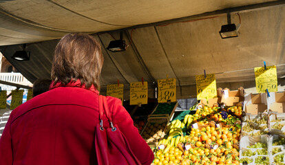 Woman at outdoor market with fresh fruit under a tent, lively atmosphere and clearly visible price tags, in a square in the historic center of Padua, Italy
