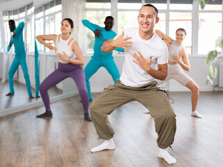 Expressive Asian guy honing hip-hop dance moves in mirrored choreographic studio setting during group training