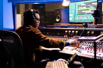 African american sound producer uses compressor and mixer in professional recording studio,...