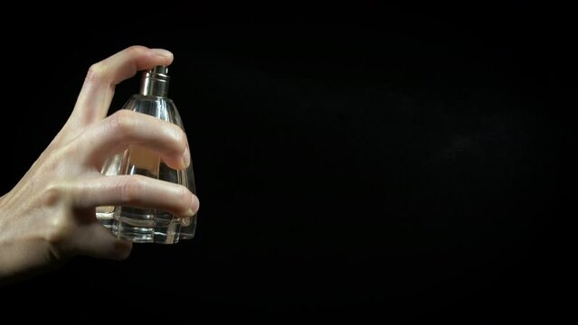 Lady spray perfume on black background. A lady hand hold the small bottle of perfume and spray it in the air on the black background.