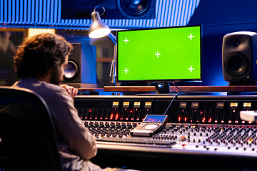 Sound engineer working with isolated display in studio control room, pushing buttons and sliders to...