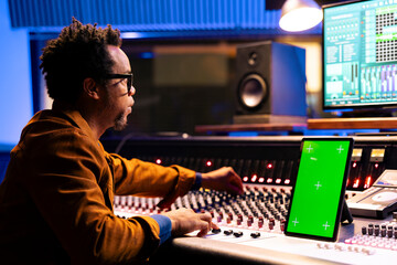 African american music producer recording and editing tracks in studio, operates panel board next...