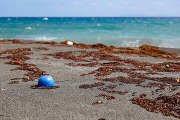 A blue plastic construction worker's hat that has been washed up on a tropical beach - the beautiful blue ocean can be seen in the background.  This demonstrates the plastic pollution in the oceans.  
