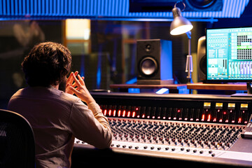 Focused sound designer processing and creating tunes in control room at professional studio,...