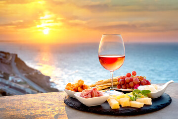 Verschiedene mediterrane Vorspeisen mit Wein, im Hintergrund Meer im Sonnenuntergang 