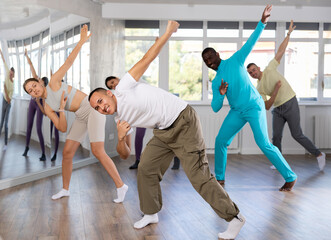 Cheerful young Asian man practicing modern street dancing during group class in choreographic studio..