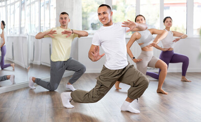 Expressive Asian guy honing hip-hop dance moves in mirrored choreographic studio setting during...