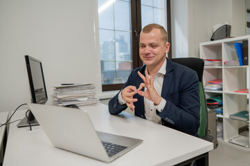 Caucasian deaf man talking sign language over video call on laptop in office.