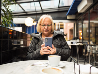 pov senior woman looking at cell phone with coffees already finished
