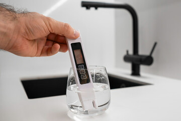 Man hand immerses conductometer in a beaker of water to check purity in front of a modern kitchen...