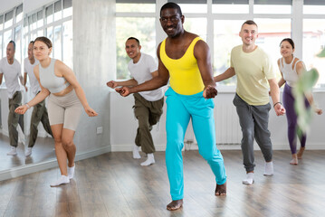 African man teaches sequences of movements, actions during dance lesson, trains to doing elements of contemporary dance, enjoys active hobby. Multinational group rehearsal, dance choreography coach