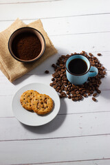Freshly brewed coffee cup, homemade cookie and freshly ground coffee on white wooden background.