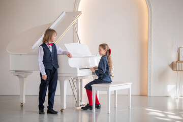 Two children play the piano and sing in a white room.