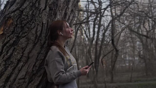 Girl standing in nature by a tree with a phone 