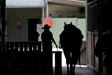 Silhouette of Australian cowgirl and a horse in a stable