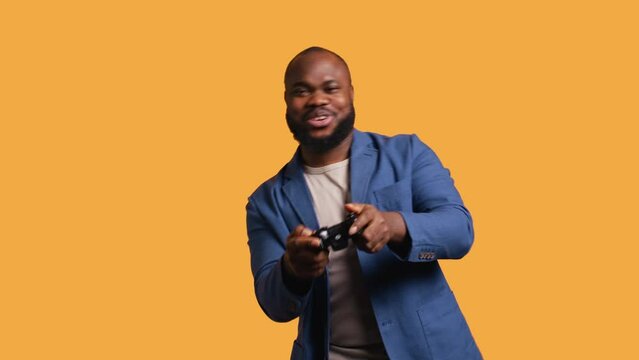 Joyous BIPOC gamer celebrating after winning gaming console game, studio background. Delighted man bragging after being victorious in videogame, defeating all enemies using gamepad, camera B