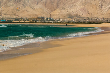 Seaside view in Bushehr, Iran with a background of refinery facilities and mountains.