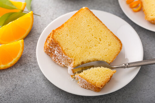Orange pound cake slice on a plate, bundt cake topped with powdered sugar