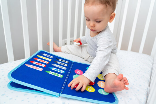 Little baby girl playing with busy book while sitting in crib. Concept of quiet books and modern educational toys