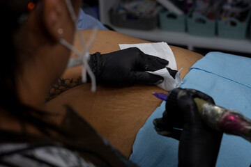 Tattoo artist covering a woman's stretch marks with ink