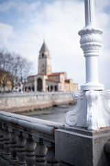 Gijón's monumental church overlooks serene beach, framed by white seaside railing, coastal beauty.