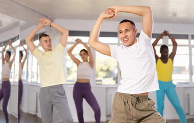 Fototapeta na wymiar Young Asian male instructor in casual sportswear enthusiastically guiding diverse class through zumba routine in fitness studio, emphasizing fun and rhythm..