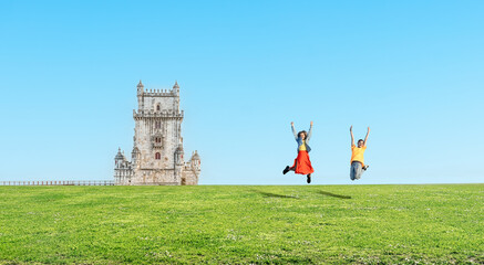 Lisbon - Portugal - Two happy young tourist girls on summer vacation jumping isolatedon a blue sky  - Woman traveler raised arms having fun at Belem Tower in Lisboa - Travel concept