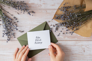 RELAX REFRESH RECHARGE text on supportive message paper note reminder from green envelope. Flat lay composition dry lavender flowers. Concept of inner happiness, slowing-down digital detox 