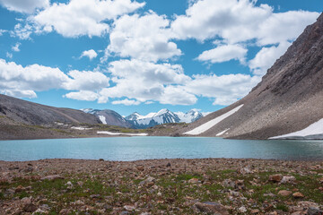 Most beautiful view to azure alpine lake against snow-covered range with few pointy peaks. Ripples on turquoise water of mountain lake against three snowy peaked tops under clouds in cloudy blue sky. - 785784940