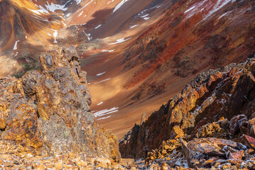 Scenic dizzying top-down view from pass into abyss. Closeup of colorful stony precipice edge with steep rocky couloir in sunlight. Large mountain wall close up. Freshly fallen snow in high mountains. - 785784941