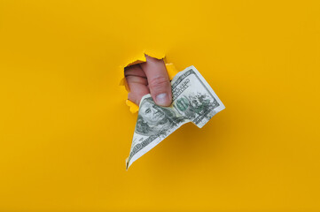 A man's hand holds dirty money through a torn hole in yellow paper. Concept of dishonest income,...