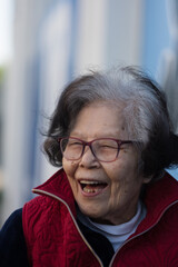 An elderly grandmother lets out a big laugh while dining outdoors. She is over ninety years old, of...