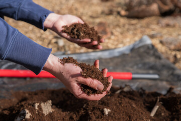Hands in rich soil compost above tarp outdoors.  Right hand in focus, closer to camera.   