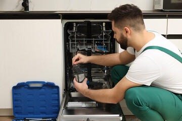 Repairman holding drain filter near dishwasher in kitchen