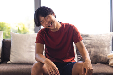 Asian teenage boy sitting on a couch at home, laughing during a video call