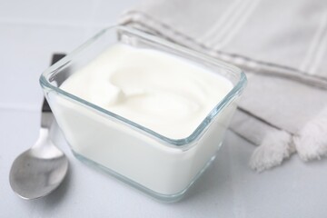 Delicious natural yogurt in glass bowl and spoon on white table, closeup