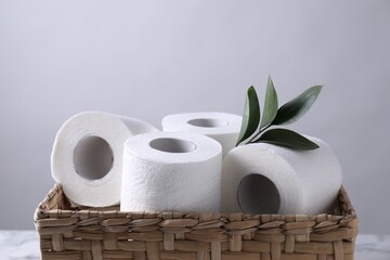 Toilet paper rolls and green leaves in wicker basket against light grey wall