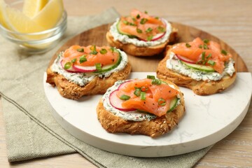 Tasty canapes with salmon, cucumber, radish and cream cheese on wooden table
