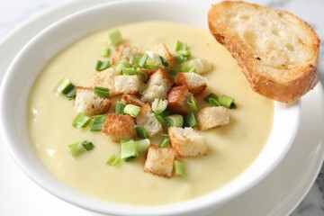 Tasty potato soup with croutons and green onion in bowl on white table