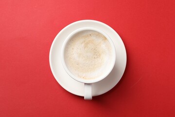 Cup of aromatic coffee on red background, top view