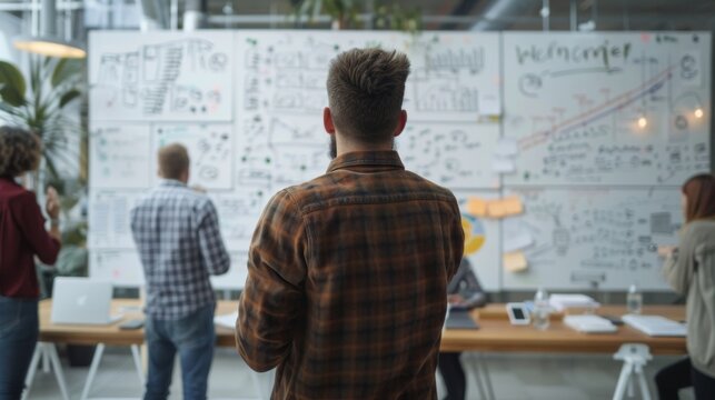 In a bustling office environment an IT professional stands in front of a whiteboard surrounded by equations and diagrams as they strategize a solution to a complex problem. Their colleagues .