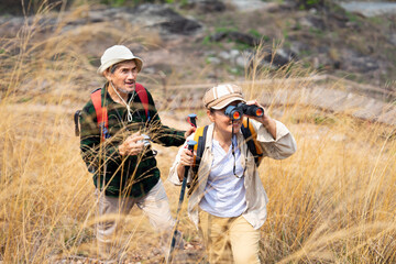 active asian senior couple hiking together on summer time,a female looking into binoculars and smiling,concept of elderly pensioner lifestyle,family relationship,activity,travel,adventure in nature