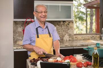Portrait of an older adult man cooking in his home kitchen. - obrazy, fototapety, plakaty